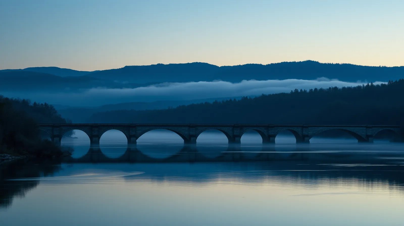 A stone arch bridge over still water at dusk in Franklin County, Massachusetts